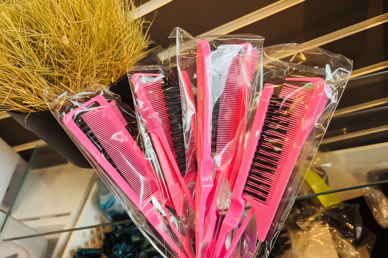 Pink hairbrushes and combs in clear packaging on a glass shelf.